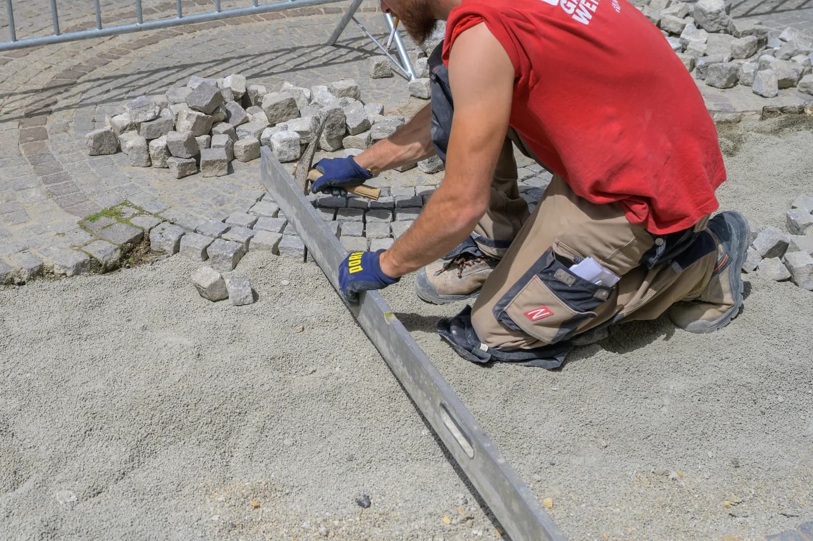 Illustration : paveur à genoux réglant des pavés de pierre avec une longue règle, sur un lit de sable