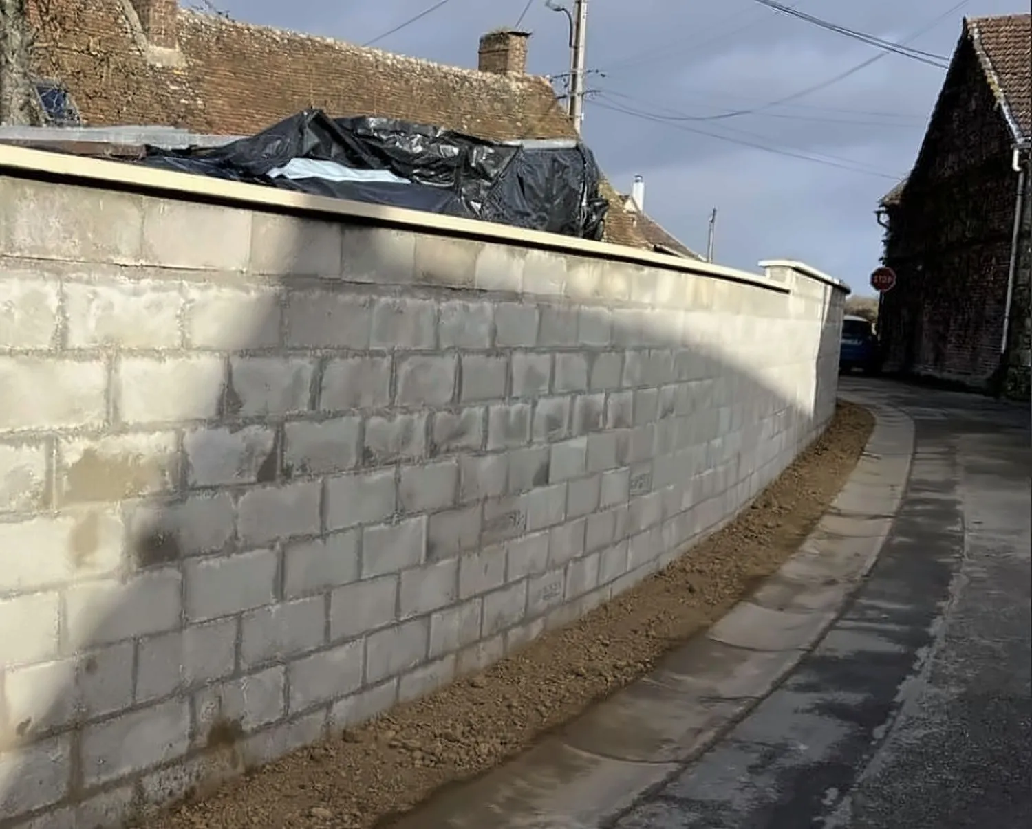 Long mur de clôture en blocs béton monté par Bouthors Couverture, qui suit la courbe d’une rue de village