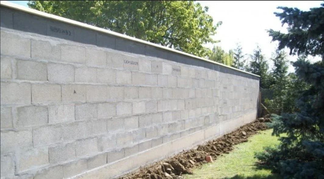 Mur de clôture en parpaings monté par Bouthors Couverture le long d’un jardin bordé de conifères