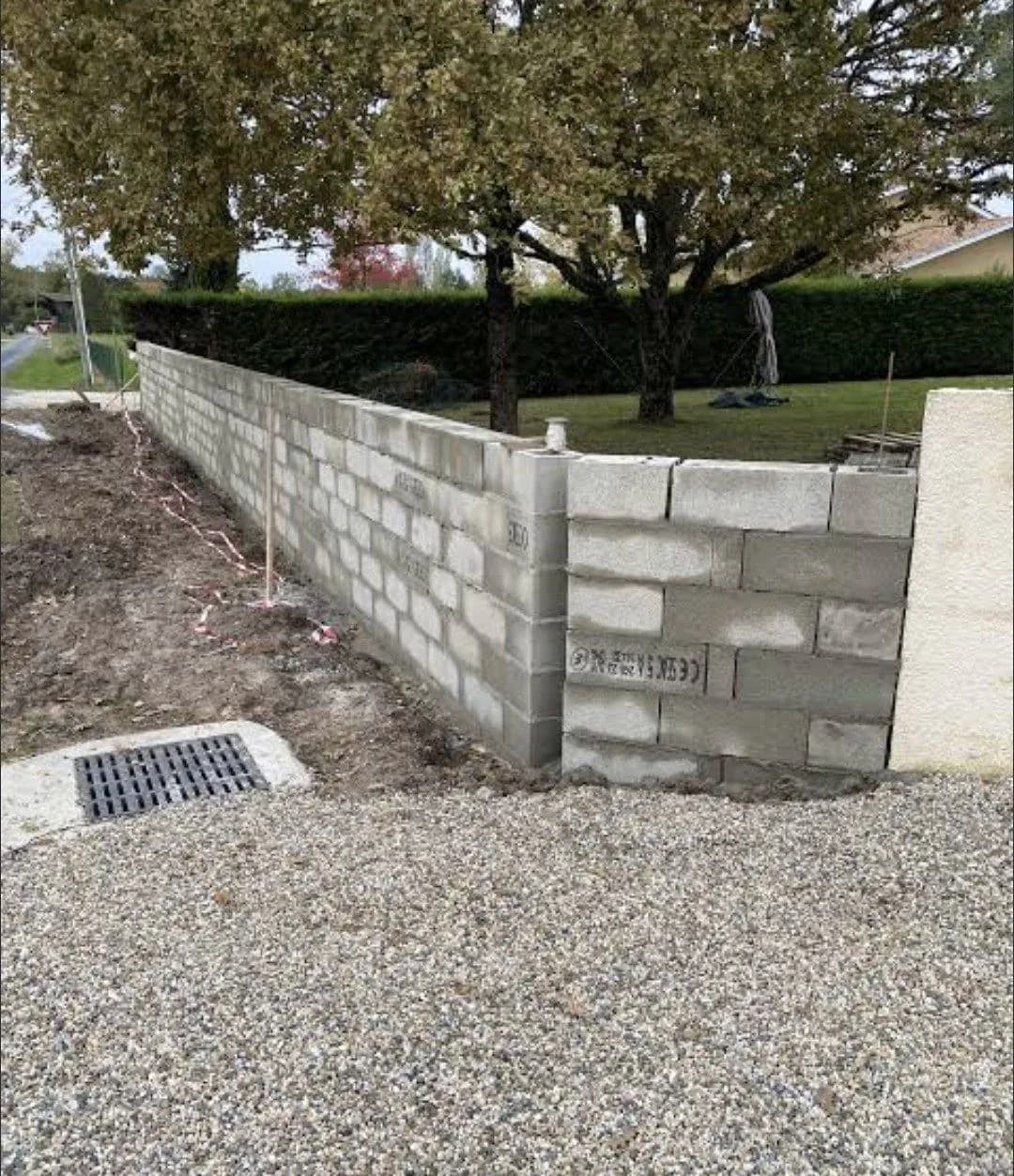 Muret en blocs béton et caniveau à grille posés par Bouthors Couverture devant une haie, sol en gravier
