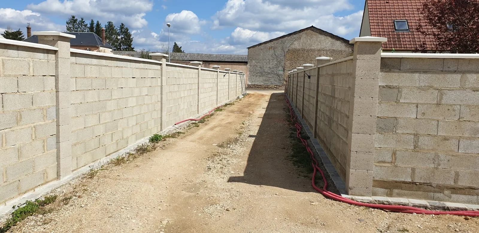 Allée en terre bordée de deux murs de clôture en blocs béton à pilastres, montés par Bouthors Couverture
