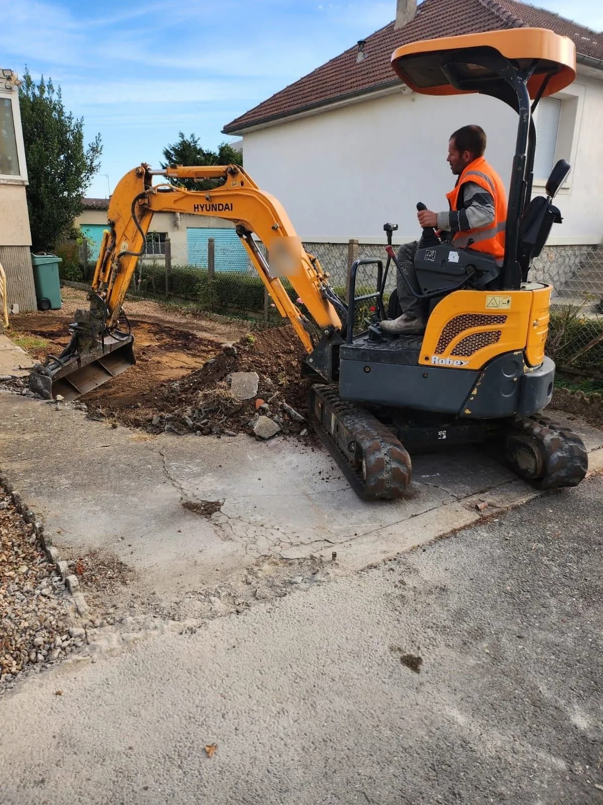 Mini-pelle décaissant l’allée d’une maison, terres et béton cassé déposés sur le côté, chantier de SJ Rénovation, partenaire de Bouthors Couverture