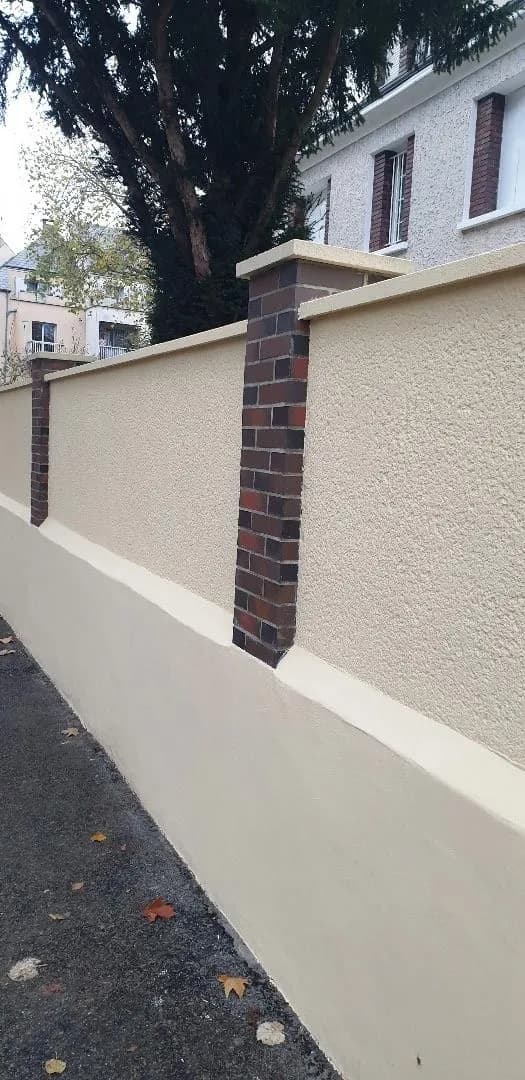 Muret ravalé, enduit clair et soubassement, pilier en brique le long d’un trottoir, chantier de SJ Rénovation, partenaire de Bouthors Couverture