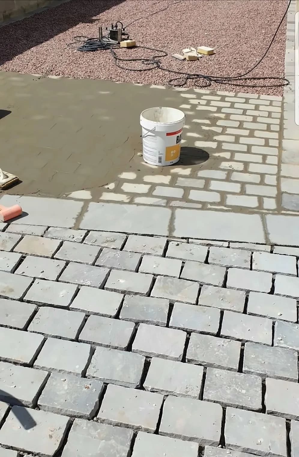Pavés gris posés à joints décalés par Bouthors Couverture, seau de mortier sur la forme