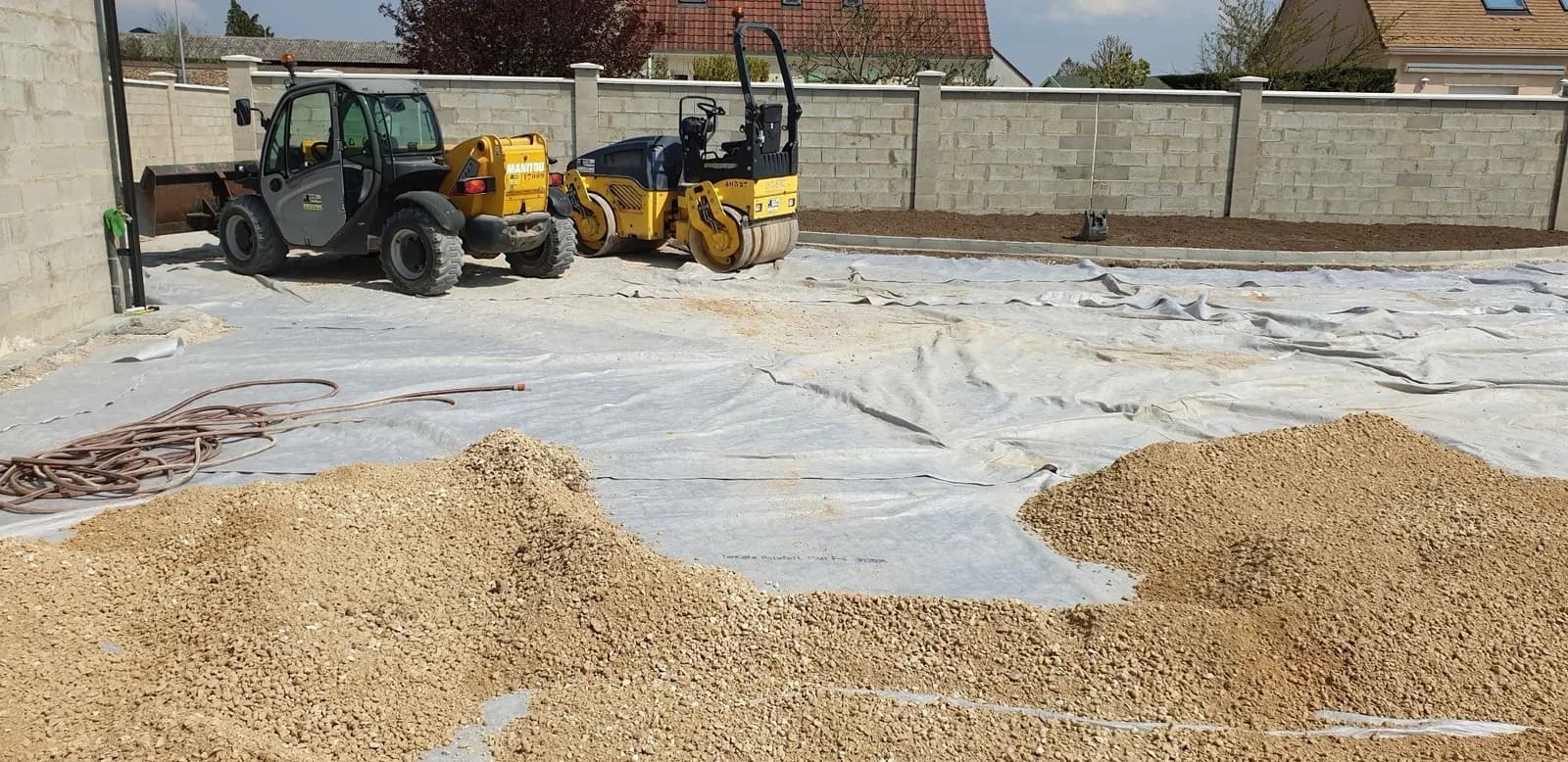 Chariot télescopique et rouleau compacteur sur la plateforme en géotextile d’une cour préparée par Bouthors Couverture